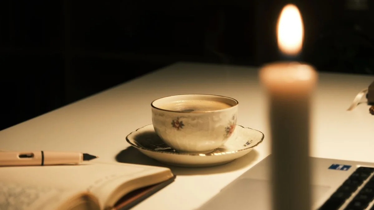 A notebook and pen beside a cup of tea and a lit candle