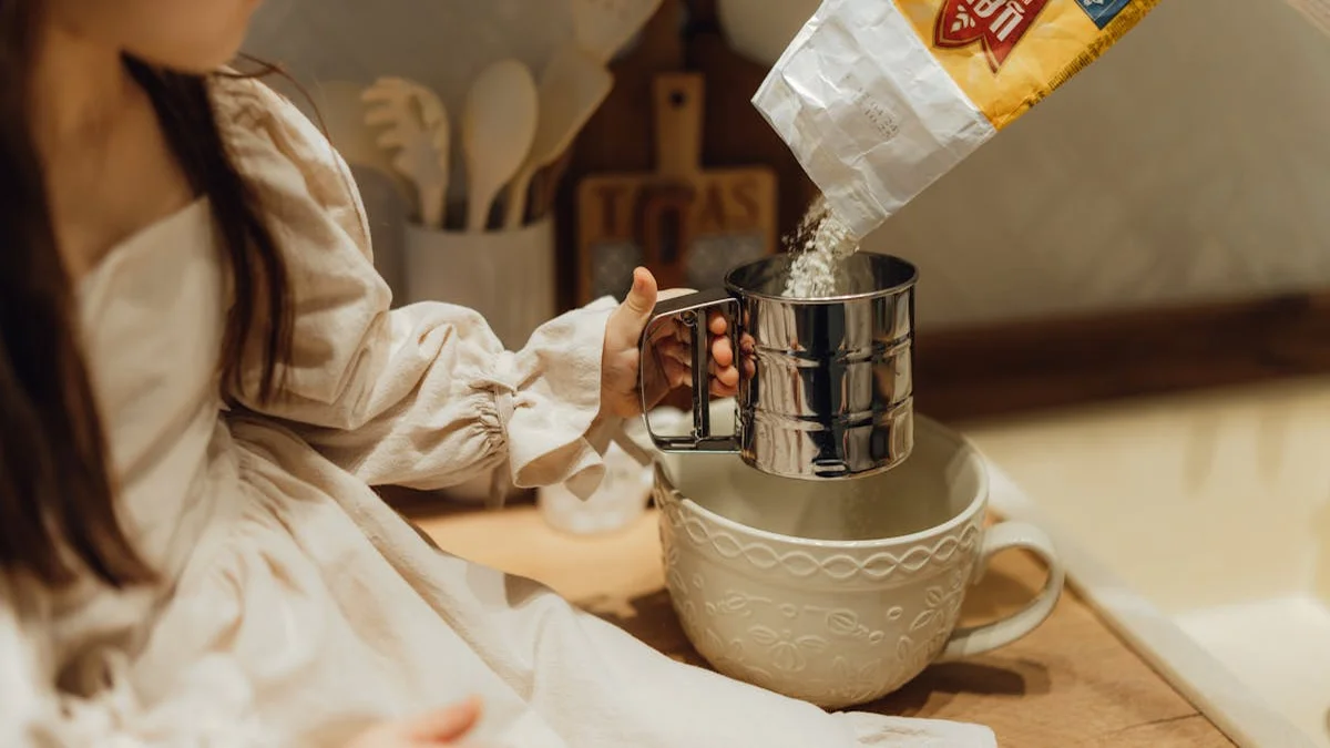 A child carefully leveling flour in a measuring cup